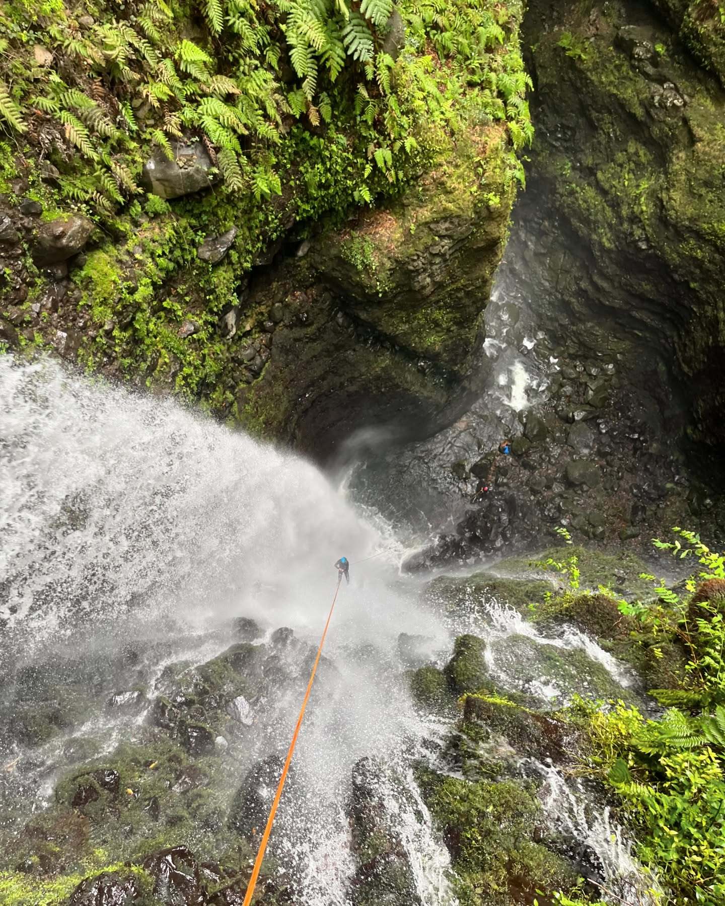 Overhead view of a canyoner on an orange rope abseiling under a waterfall in Ribeira Funda, Madeira