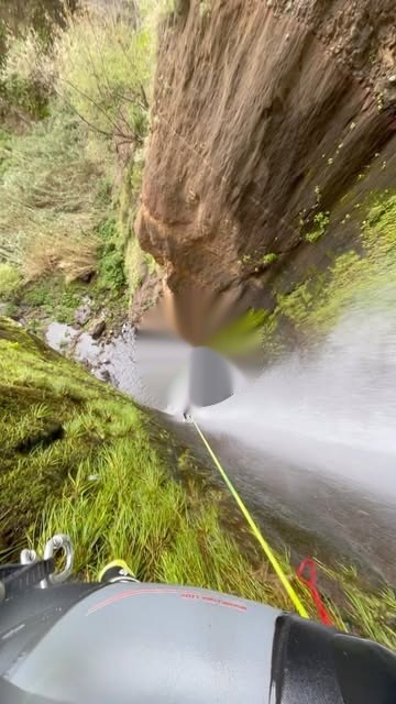 POV canyoning in Madeira — abseiling down a waterfall on rope with harness, lush green canyon walls