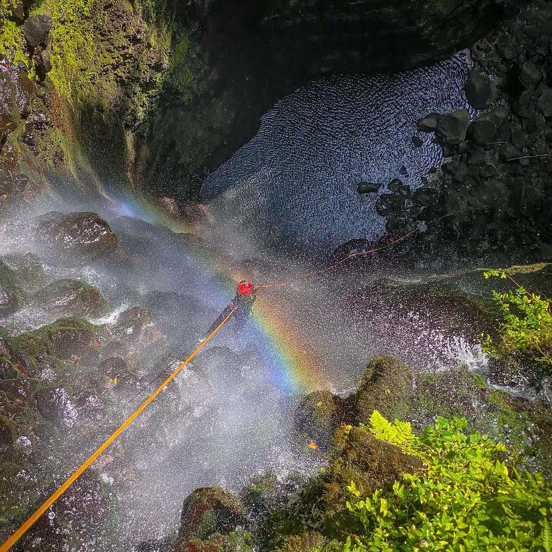 Canyoneer rappelling a waterfall in Madeira with a rainbow in the spray