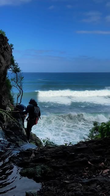 Two hikers on a coastal cliffside with ocean waves in the background.