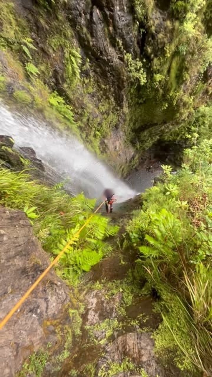 Person rappelling down a mossy cliff beside a waterfall.
